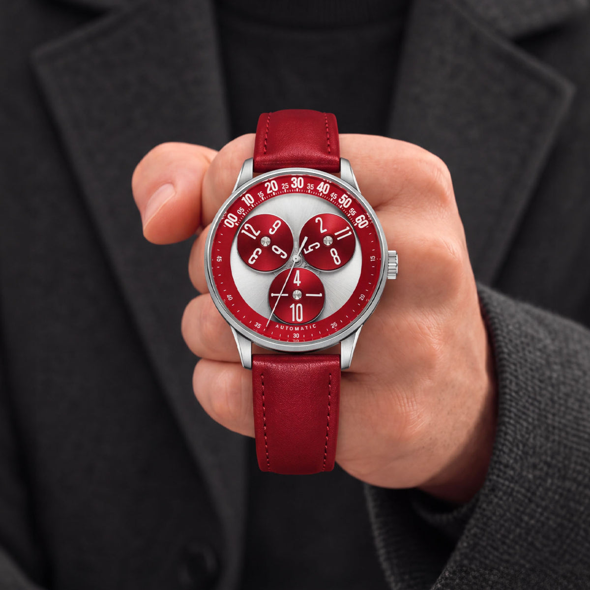 Mandetbrote Wandering Hour Burgundy — Held in hand against a charcoal jacket, showing the hour discs and central seconds hand, available at IFL Watches.