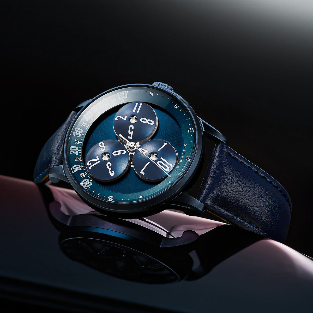 Mandetbrote Wandering Hour Dark Blue — Angled on a reflective surface, showing the case and crown, available at IFL Watches.